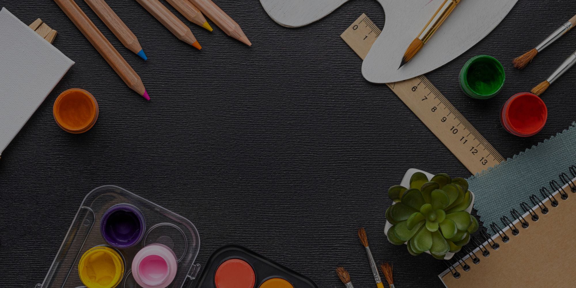 Art supplies including pencils, paint pots, and a notebook on a dark surface.

