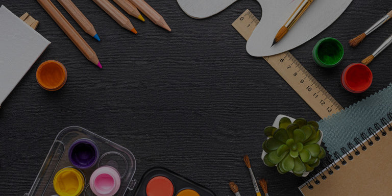 Art supplies including pencils, paint pots, and a notebook on a dark surface.

